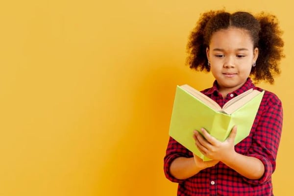 Niña aplicando las estrategias de lectura con un libro amarillo